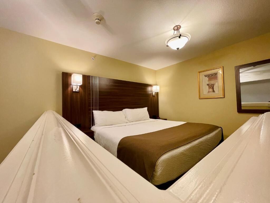 Une chambre d’hôtel avec un lit, des lampes de chevet, un tableau encadré au mur et un luminaire au plafond.