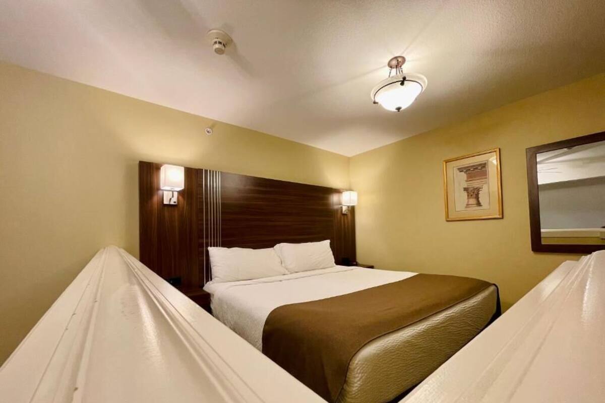 Ein Hotelzimmer mit Bett, Nachttischlampen, einem gerahmten Bild an der Wand und einer Deckenleuchte.