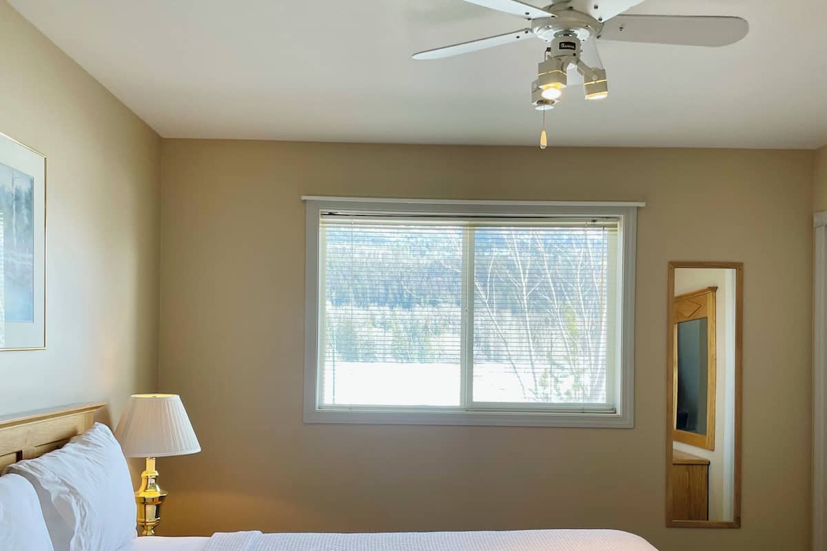 Ein Schlafzimmer mit einem großen Bett, einem Deckenventilator, einem Fenster und einer Nachttischlampe.