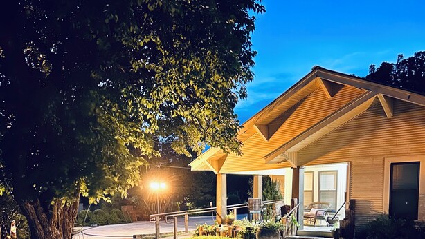 Ett modernt hus med en inglasad veranda, ett stort träd och en välskött gräsmatta.