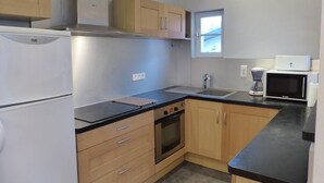 A compact kitchen with a refrigerator, oven, microwave, and a small window. - Apartment in villa "AIRE ONA" between lake and ocean for 4 people (Soorts-Hossegor)
