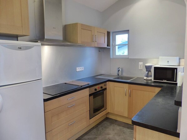 A compact kitchen with a refrigerator, oven, microwave, and a small window. - Apartment in villa "AIRE ONA" between lake and ocean for 4 people (Soorts-Hossegor)
