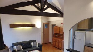 A compact living space with a black leather sofa, a small wooden table, and a kitchen area with wooden cabinets and a white refrigerator. - Apartment in villa "AIRE ONA" between lake and ocean for 4 people (Soorts-Hossegor)