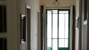 A hallway with wooden flooring, a green door, and a hanging light fixture.