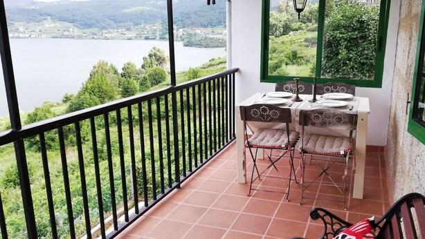 A balcony with a table set for two, overlooking a lake and hills.