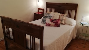 A neatly made bed with a wooden headboard, a bedside table with a lamp, and a small round table with a book.