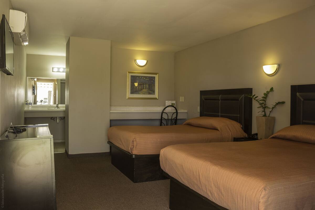 Ein Hotelzimmer mit zwei Betten, einem Schreibtisch, einem Spiegel, einem Nachttisch und einem Wandbild.