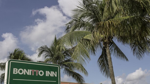 A sign for Bonitto Inn Hotel with a view of palm trees and a building with a red roof in the background. - BONITTO INN® Tampico Altamira (Altamira)
