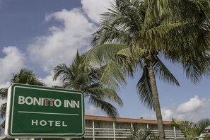 Naamplaatje voor Hotel Bonitto Inn, met uitzicht op palmbomen en een gebouw met een rood dak op de achtergrond.