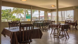 A restaurant with multiple tables and chairs, large windows with a view of palm trees and buildings, and a sign for Bonito Hotel. - BONITTO INN® Tampico Altamira (Altamira)