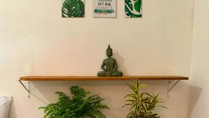 Una habitació amb un llit, una estanteria amb una estàtua de Buda i dues plantes en testos sobre tamborets de fusta.
