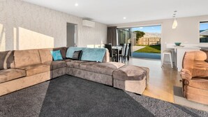 Een moderne woonkamer met een modulaire bank, een eethoek en een keuken die door een open deur zichtbaar is.