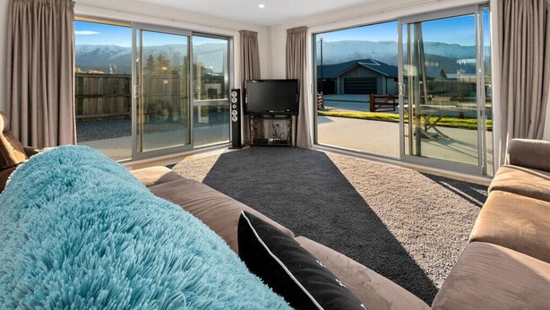 Een moderne woonkamer met een grote bank, een flatscreen-tv en uitzicht op bergen door grote schuifdeuren.