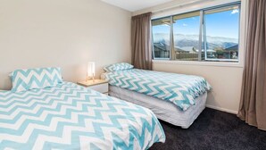 Een slaapkamer met twee bedden, een nachtkastje, een raam met gordijnen en uitzicht op bergen.