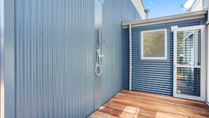 A compact outdoor area with a wooden deck, a metal wall, and a sliding glass door leading to a balcony.