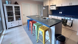 A modern kitchen with a central island, stainless steel appliances, and colorful stools.