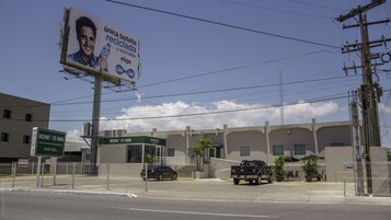 Un hotel con recepción, estacionamiento cercado y un cartel publicitario de una bebida.