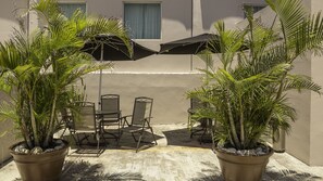 An outdoor seating area with two potted palm trees, a table, and two chairs. - BONITTO INN® Tampico Aeropuerto (Tampico)