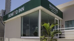 Zona de recepción de BONITTO INN con fachada de vidrio transparente, un mostrador de recepción y un letrero dando la bienvenida a los huéspedes.