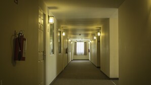 Un largo y estrecho pasillo de hotel con puertas a ambos lados, un extintor en la pared izquierda e iluminación en el techo.