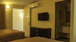 Habitación de hotel con dos camas, un televisor montado en la pared, un escritorio con cajones y un baño visible a través de una puerta abierta.
