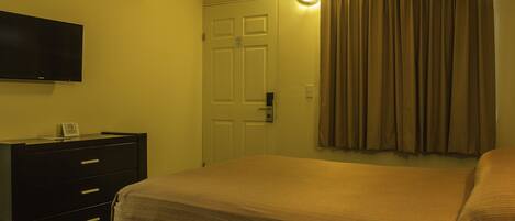 A hotel room with a bed, a dresser, a television, and an air conditioning unit.