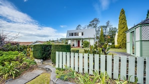 A residential property with a well-maintained garden, a white picket fence, and a house with a grey roof. - Jacaranda Lodge - Napier Hill Holiday Home (Napier City)