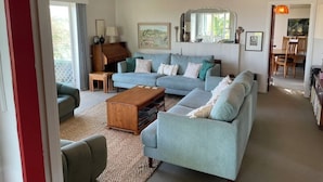 A spacious living room with a light blue sofa set, a wooden coffee table, and a large mirror above the sofa. - Jacaranda Lodge - Napier Hill Holiday Home (Napier City)