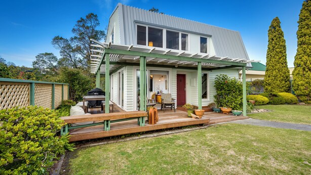 A house with a covered porch, a barbecue grill, outdoor seating, and a well-maintained lawn. - Jacaranda Lodge - Napier Hill Holiday Home (Napier City)