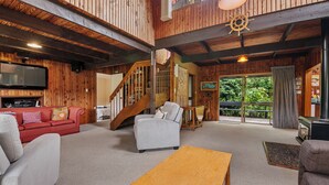 Amplia sala de estar con detalles de madera, una escalera, chimenea y un ventanal grande.