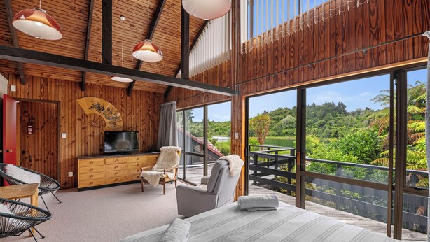 Una habitación amplia con una cama grande, televisión, armario de madera y balcón con vistas a exuberante vegetación.