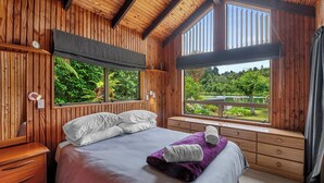 Un dormitorio con paneles de madera, una cama grande, una ventana con vistas a la vegetación y un aparador de madera.