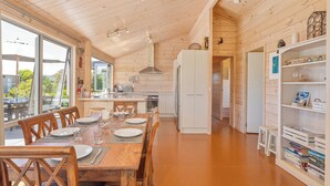 Een houten interieur met een eettafel voor vier personen, een keuken met witte apparaten en een boekenplank vol boeken.