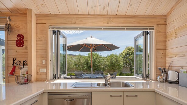 Een moderne keuken met een vaatwasser, een spoelbak en een raam met uitzicht op een terras met een parasol.