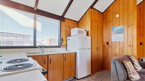 A compact kitchen with wooden walls, a refrigerator, a stove, and a window with blinds.