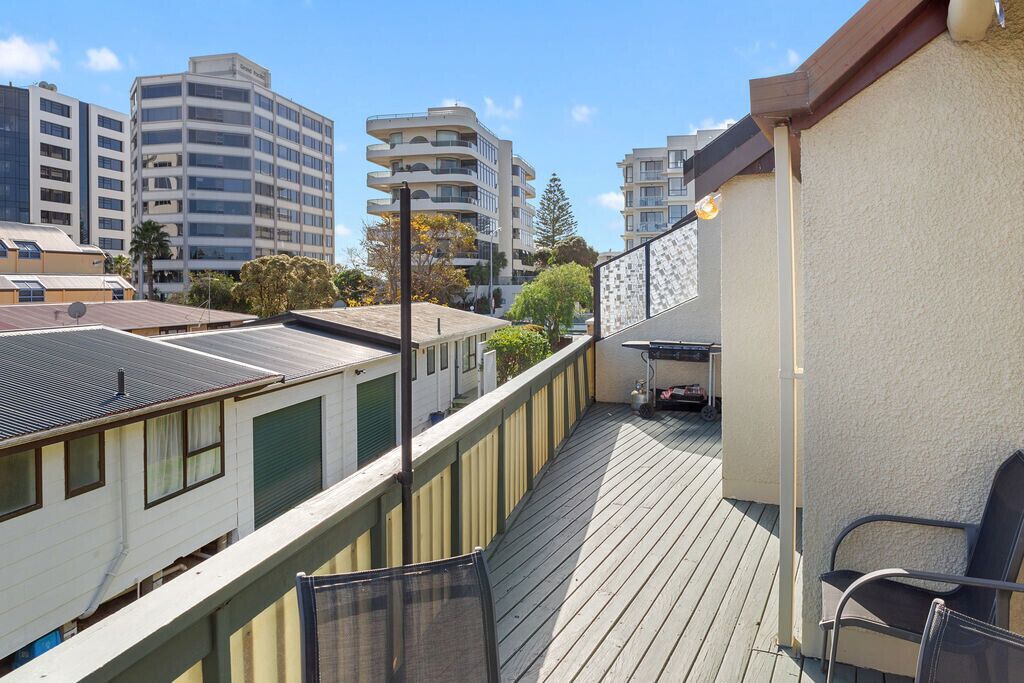 A balcony with a view of surrounding buildings, a chair, and a table.