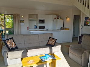 Una sala de estar con un sofá y sillones, una mesa de centro, y una cocina al fondo.