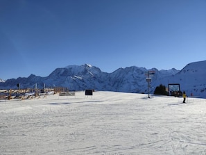 A snow-covered ski slope with a mountain backdrop, ski lift, and signage.