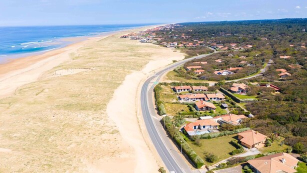 An aerial view of a coastal residential area with houses, a beach, and a road curving along the coast. - The "Maison des Moineaux" between lake and ocean for 6 persons (Soorts-Hossegor)