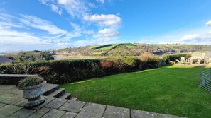 A well-maintained lawn with a stone wall and a view of rolling hills in the distance.