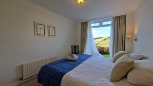 A bedroom with a bed, a window with curtains, a radiator, and framed pictures on the wall.