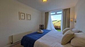 A bedroom with a bed, a window with curtains, a radiator, and framed pictures on the wall. - 2 Steepfield, spacious apartment, Bantham S. Devon (Bantham)