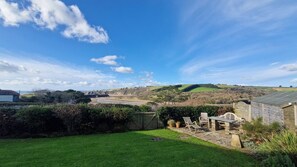 A rural landscape with a grassy lawn, a wooden fence, and a view of a beach and hills in the distance. - 2 Steepfield, spacious apartment, Bantham S. Devon (Bantham)