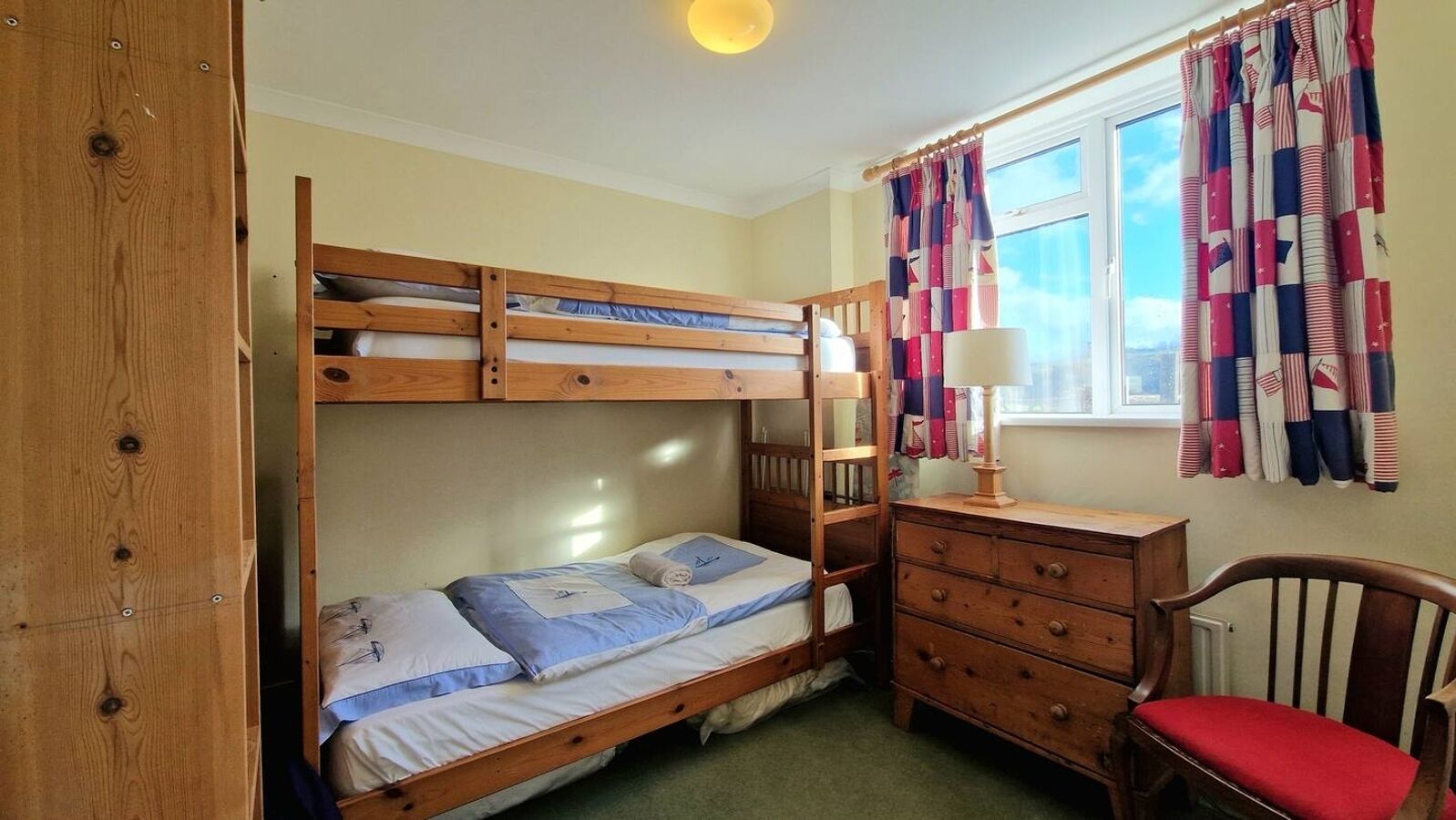 Habitación con literas, escritorio, silla, ventana con cortinas y un radiador.