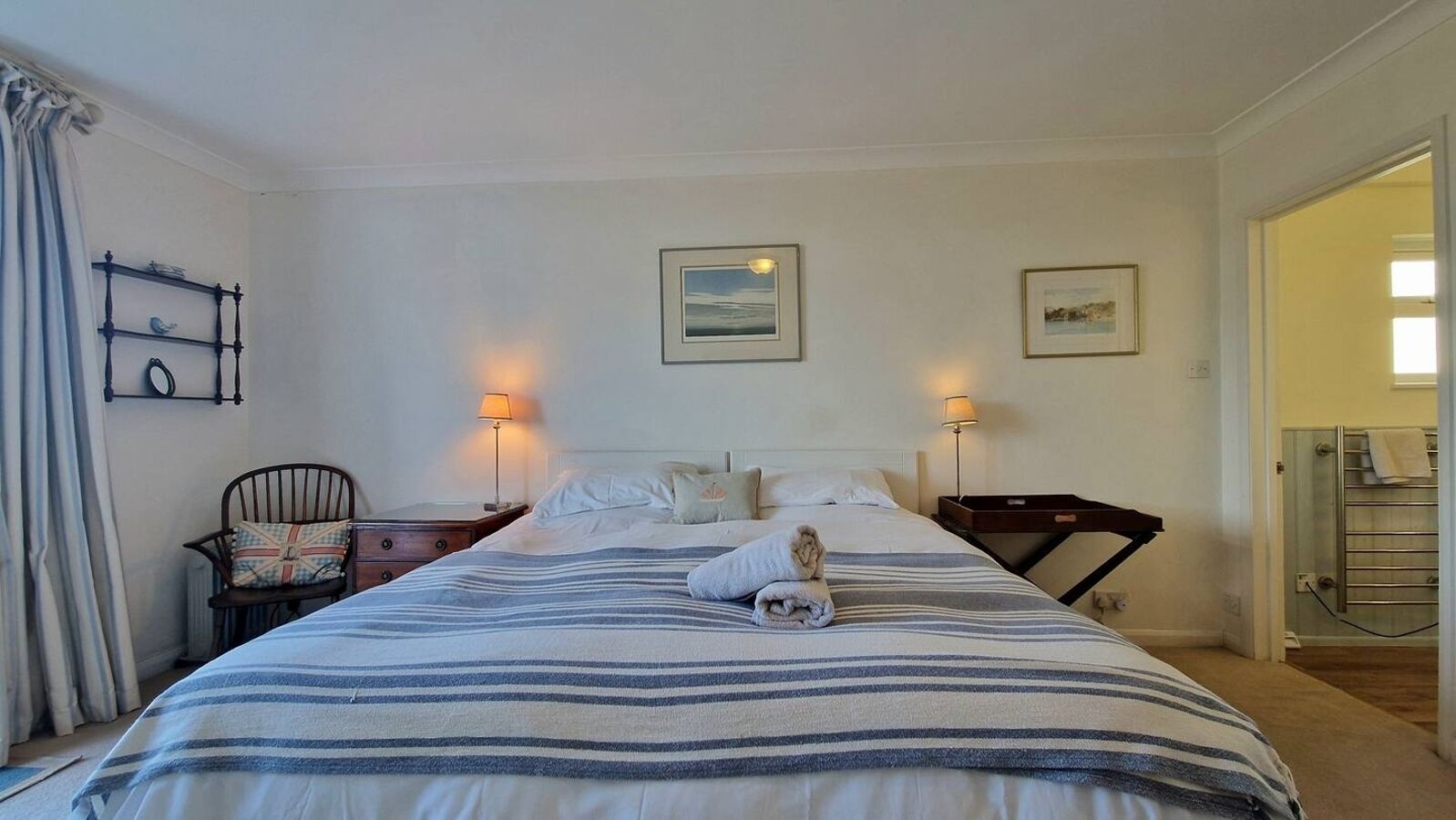 A hotel room with a large bed, two bedside lamps, a chair, a small table, and a view of the bathroom.