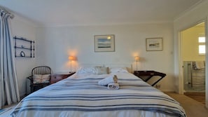 Ein Hotelzimmer mit einem großen Bett, zwei Nachttischlampen, einem Sessel, einem kleinen Tisch und Blick ins Bad.