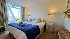A hotel room with a bed, bedside tables, a window with curtains, and a wall-mounted lamp.