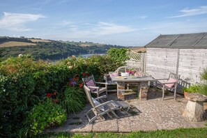 Eine Terrasse mit Tisch und Stühlen, umgeben von üppiger Vegetation und Blick auf sanfte Hügel.