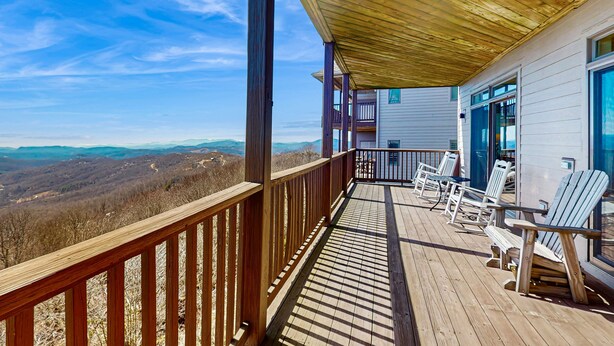 Eine Holzterrasse mit Bergblick, eine überdachte Veranda und ein Gebäude mit großen Fenstern.