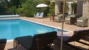 A swimming pool with lounge chairs and umbrellas, surrounded by greenery and stone walls. - Luxurious 3 bedroom villa with private pool garden and sea view (Kouklia)